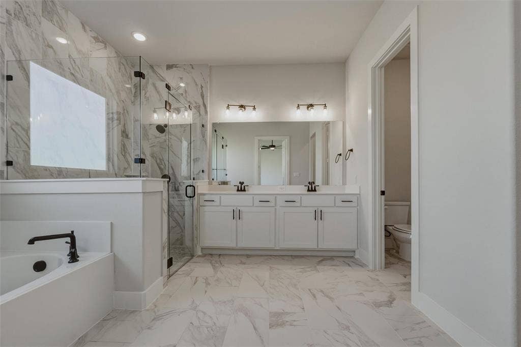 2305 Quartz Street, Krum, TX 76249 Spacious bathroom featuring a dual vanity with white cabinetry, a glass-enclosed shower, a built-in soaking tub with a matte black fixture, and large-format tile flooring