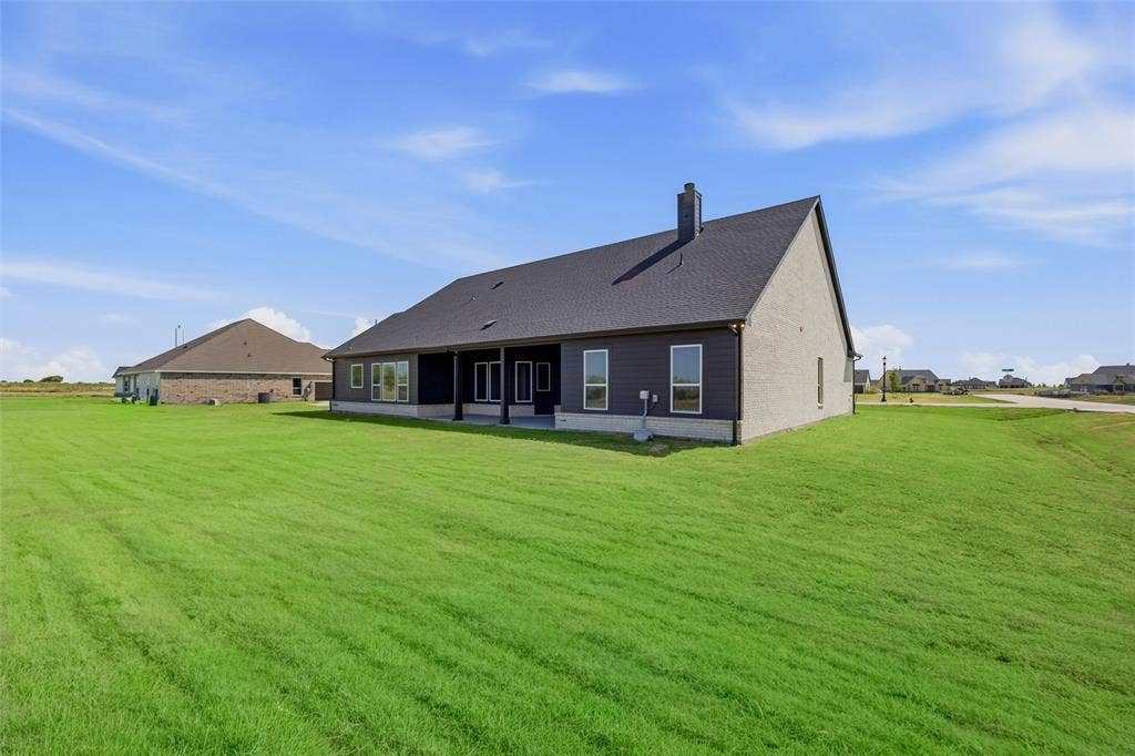 2305 Quartz Street, Krum, TX 76249 Expansive green lawn surrounding a residence with a dark shingle roof, light-colored siding, and a covered patio