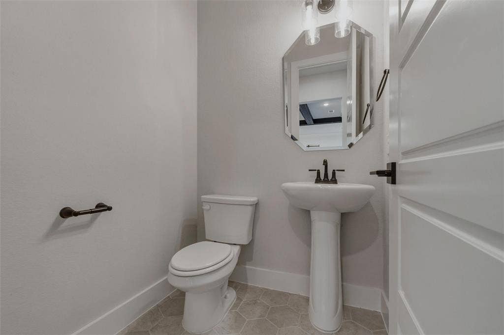 2305 Quartz Street, Krum, TX 76249 Pedestal sink with dark bronze fixtures, octagonal mirror, and light-toned hexagonal tile flooring