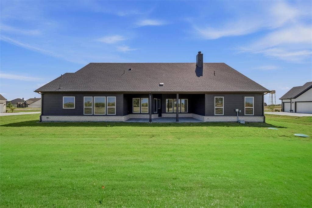 2305 Quartz Street, Krum, TX 76249 Expansive green yard with a dark shingled roof, dark siding, multiple windows, and a covered concrete patio