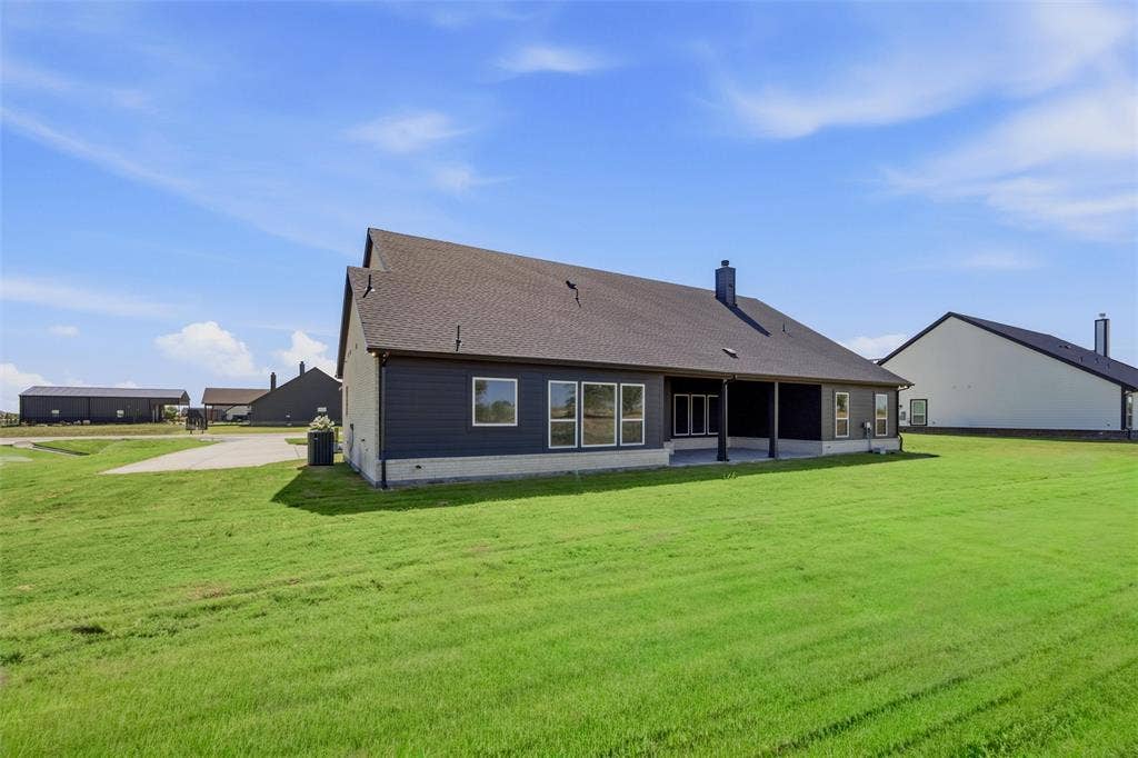 2305 Quartz Street, Krum, TX 76249 Expansive green space, dark siding with white trim, covered patio, multiple windows, and a dark shingle roof