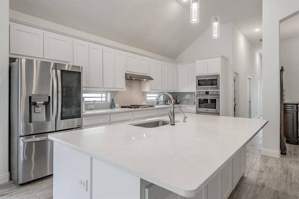 Kitchen with stainless steel appliances, an island with sink, white cabinetry, and sink