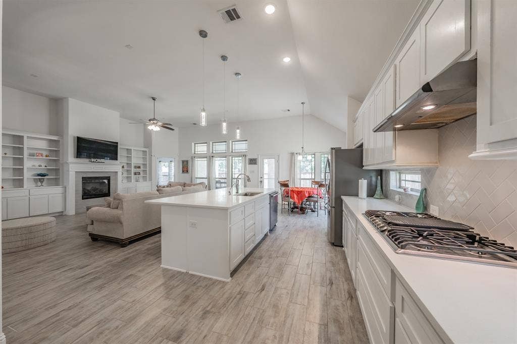 Kitchen with a kitchen island with sink, vaulted ceiling, white cabinetry, and ceiling fan