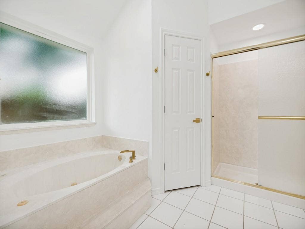 4312 Avonshire Lane, Plano, TX 75093 Soaking tub with a tiled surround, frosted window, white paneled door, and a glass-enclosed shower with gold-tone hardware