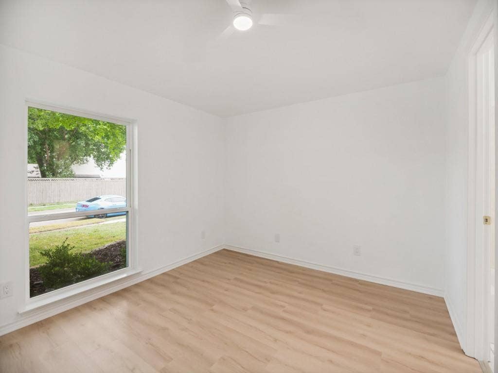 4312 Avonshire Lane, Plano, TX 75093 Bright room featuring wood-finish flooring, white walls, a ceiling fan with integrated lighting, and a large window overlooking exterior landscaping