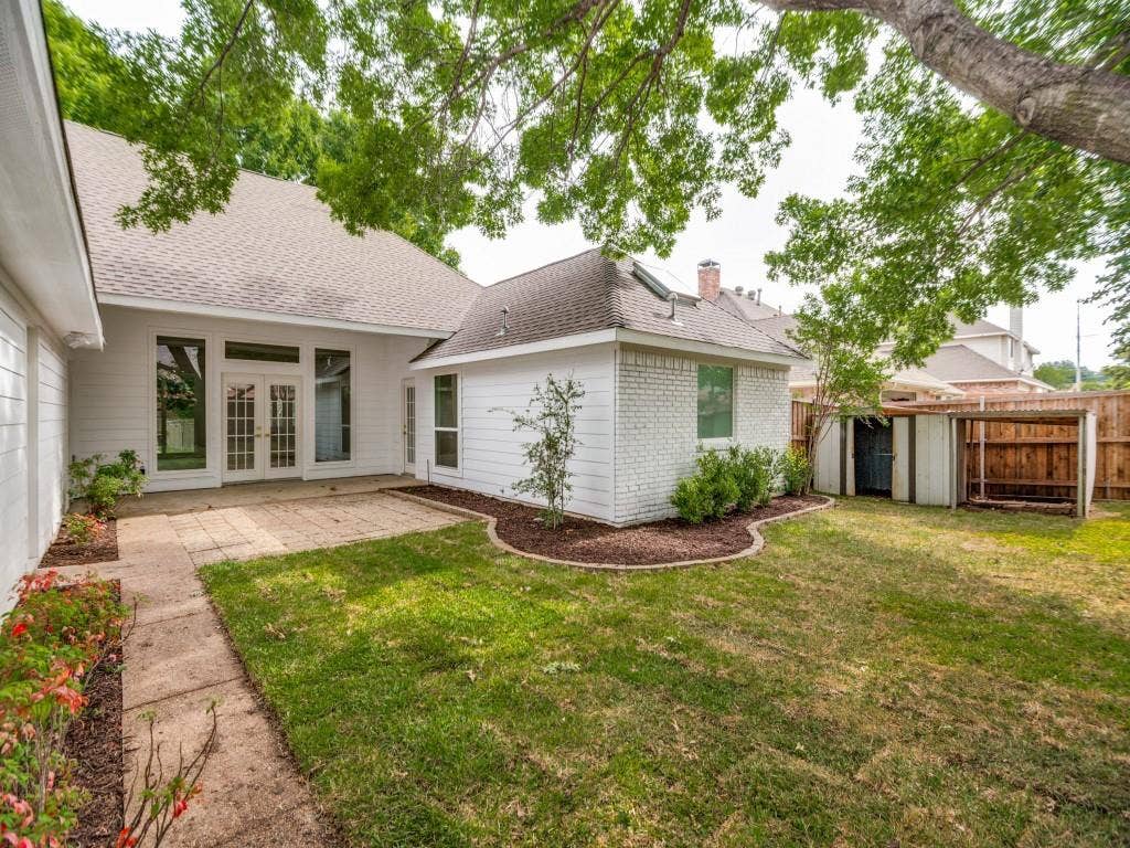 4312 Avonshire Lane, Plano, TX 75093 Rear exterior featuring white siding, a paved patio, and a grass lawn