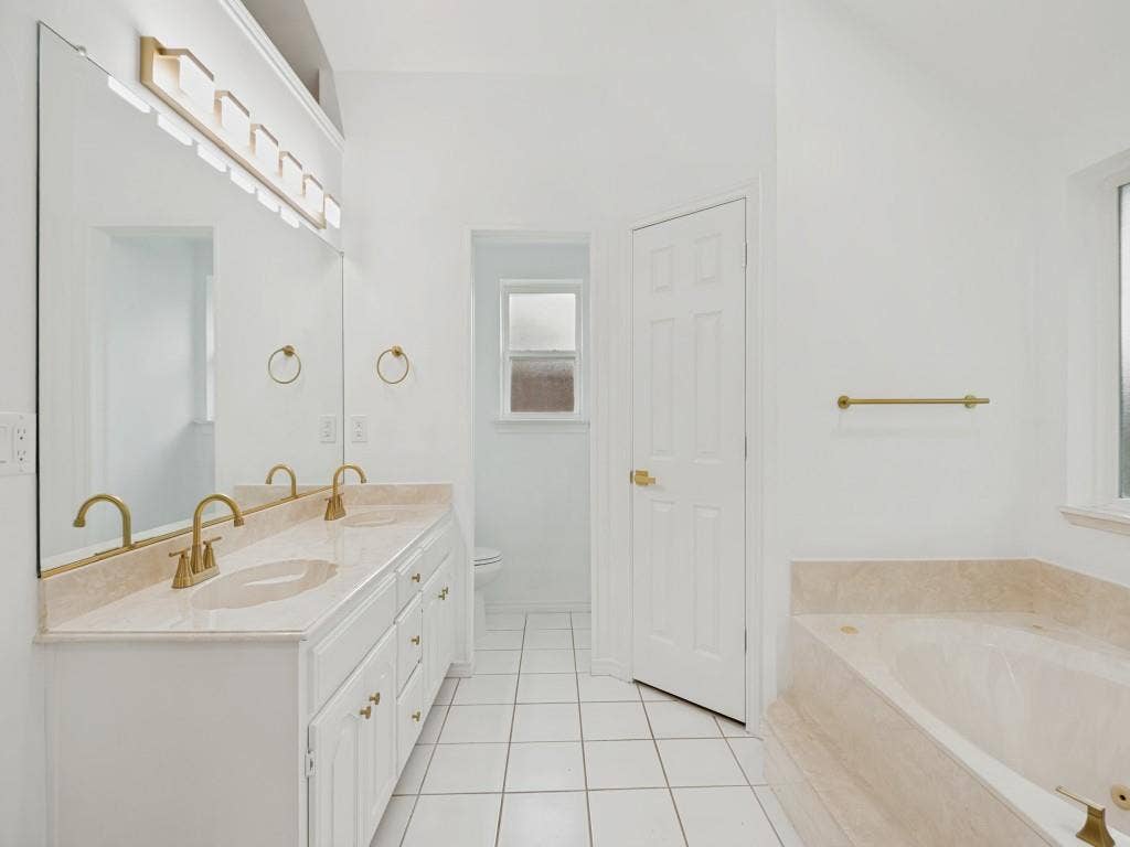 4312 Avonshire Lane, Plano, TX 75093 Bathroom featuring a double vanity with built-in sinks, light-toned countertop, and gold-finish fixtures