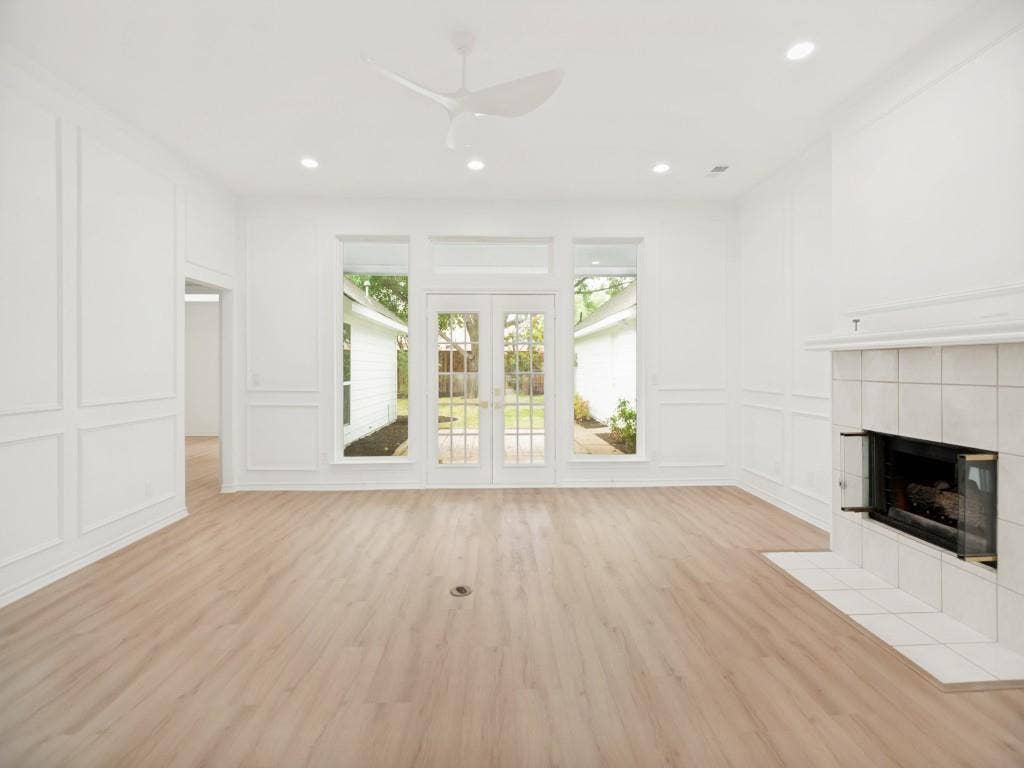 4312 Avonshire Lane, Plano, TX 75093 Light-filled living area featuring wood-finish flooring, a tiled fireplace with glass enclosure, and French doors opening to the exterior