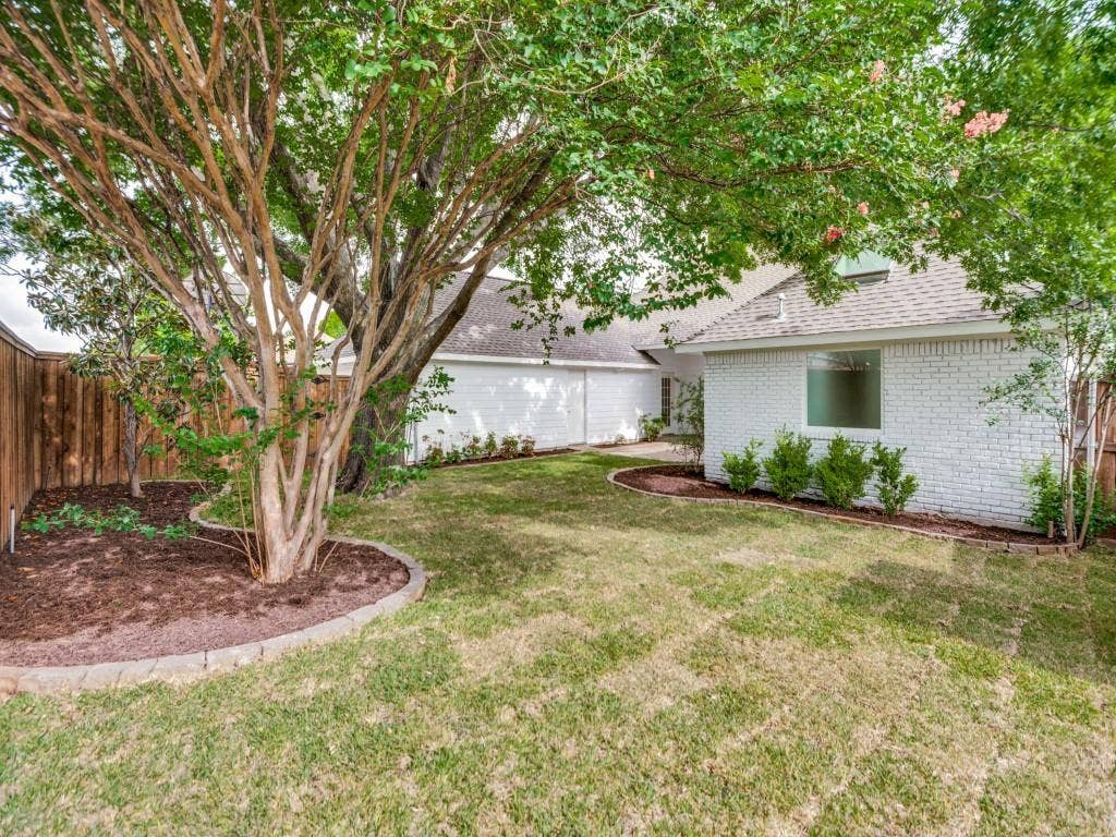4312 Avonshire Lane, Plano, TX 75093 Spacious backyard featuring a substantial tree with textured bark, a manicured lawn, and a white brick exterior