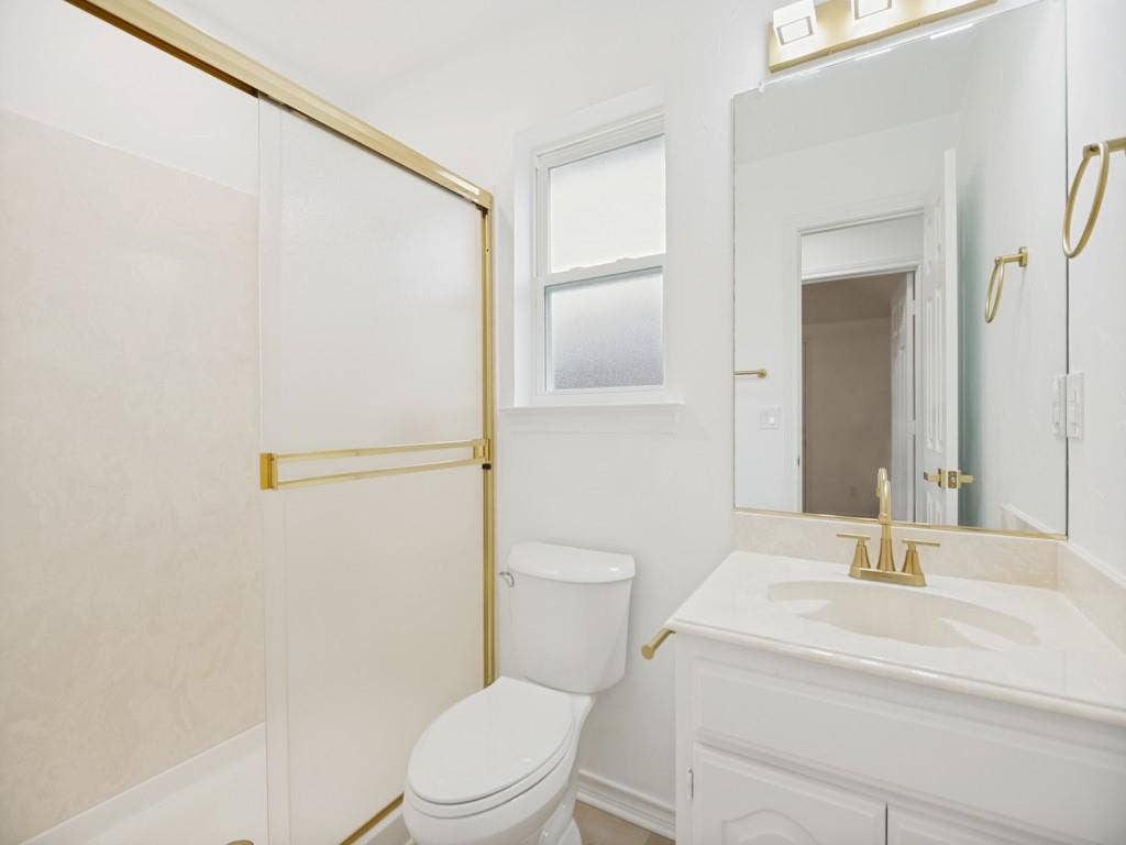4312 Avonshire Lane, Plano, TX 75093 Full bathroom featuring a shower with gold-toned sliding doors, a vanity with a drop-in sink and gold-toned faucet, a large wall-mounted mirror, and a window with privacy glass