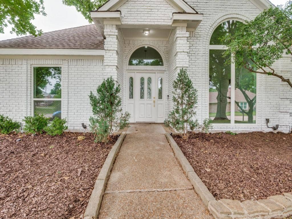 4312 Avonshire Lane, Plano, TX 75093 White brick exterior with a prominent arched entry, featuring a double door with decorative glass inserts