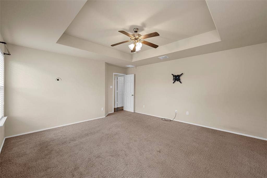 Spacious room featuring a tray ceiling with a ceiling fan, neutral wall paint, and carpet flooring
