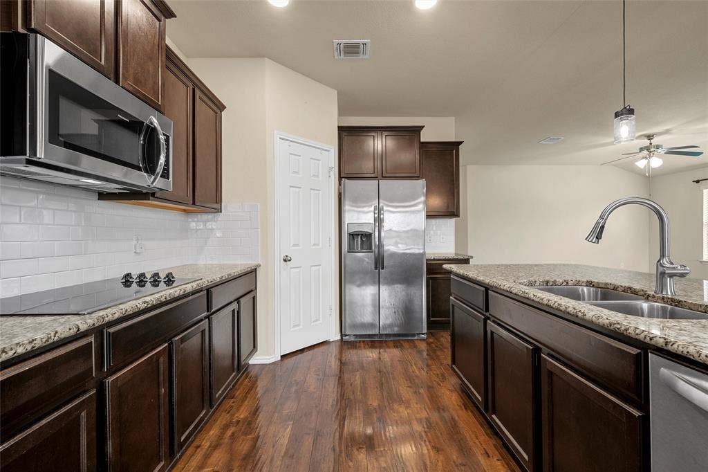 Kitchen featuring rich wood-finish flooring, dark wood cabinetry, granite countertops, and stainless steel appliances