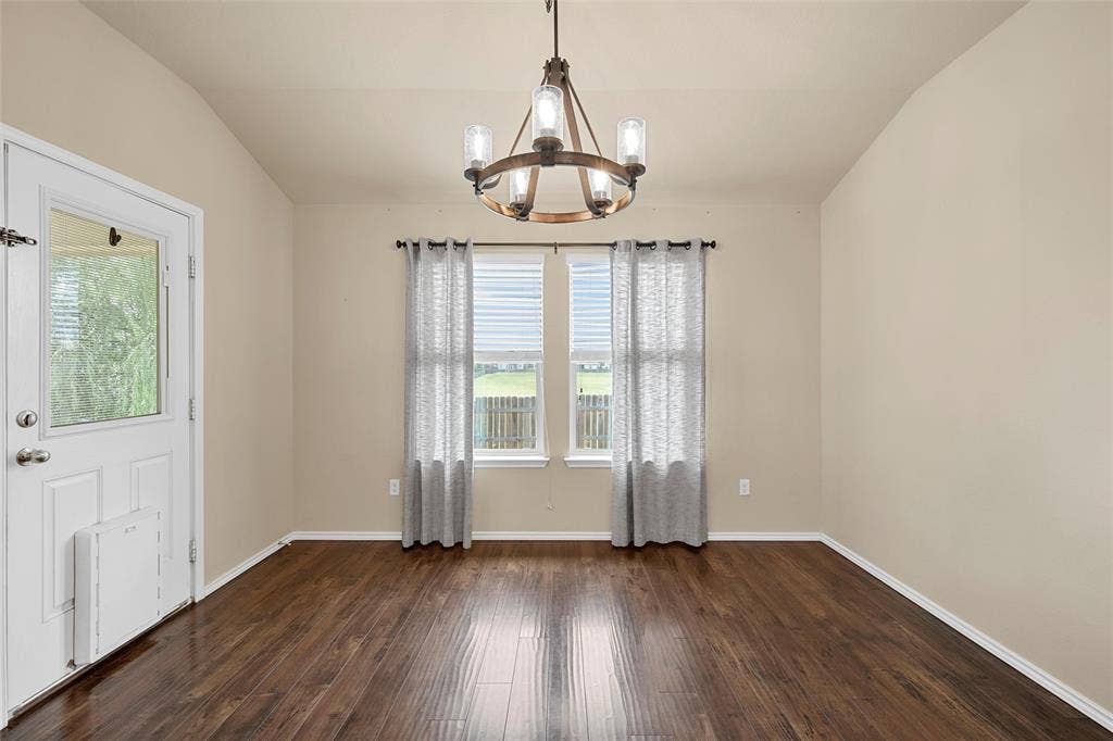 Vaulted ceiling room featuring wood-finish flooring, a rear-facing glass-paneled door, and two rear-facing windows