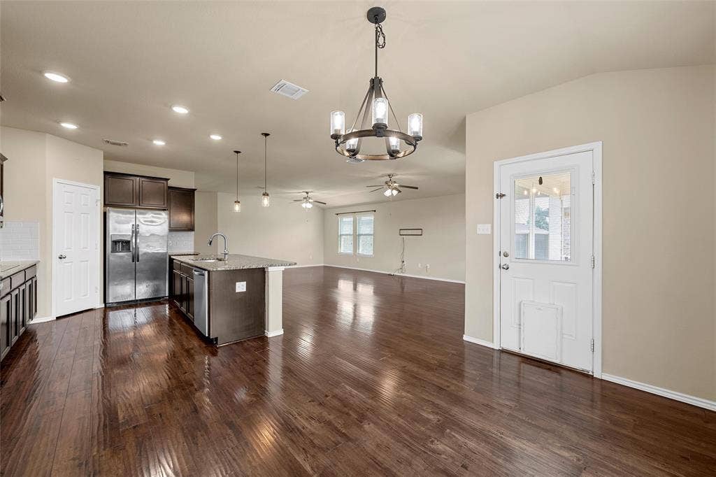 Open-concept living space featuring wood-finish flooring, a kitchen island with sink, stainless steel appliances, dark wood cabinetry, and recessed lighting