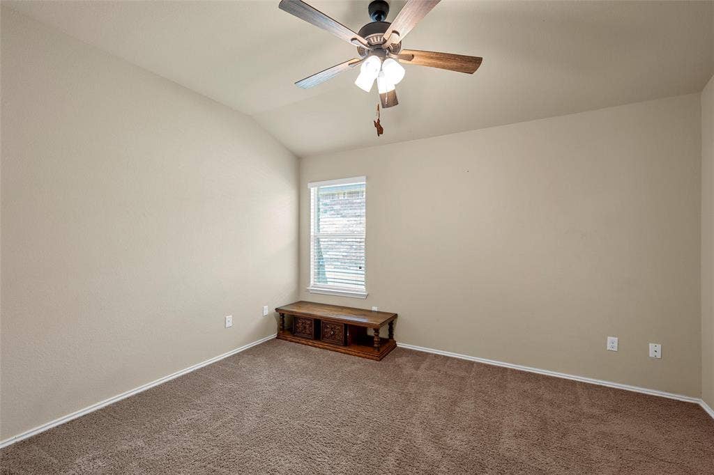 Vaulted ceiling room featuring neutral-toned walls, brown carpet, and a window with blinds