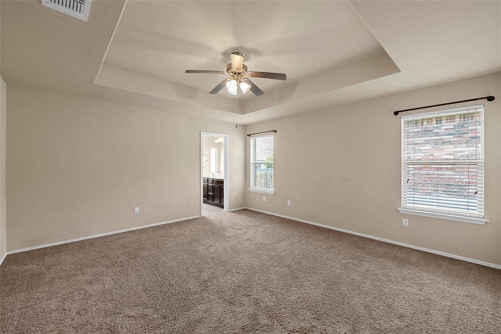 Carpeted room with a tray ceiling and ceiling fan