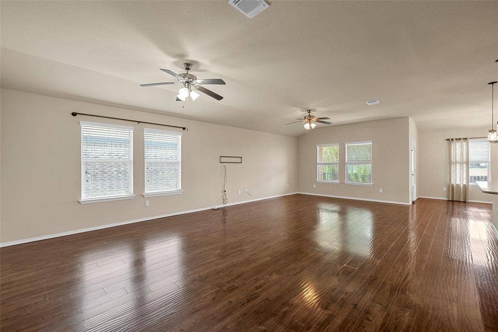 Open-concept living area featuring wood-finish flooring, neutral wall tones, and multiple windows with blinds