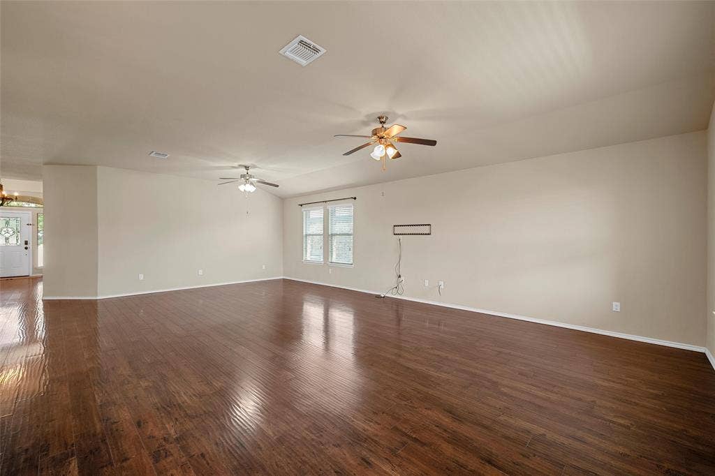 Spacious living area featuring wood-finish flooring, two ceiling fans, and multiple windows providing natural light