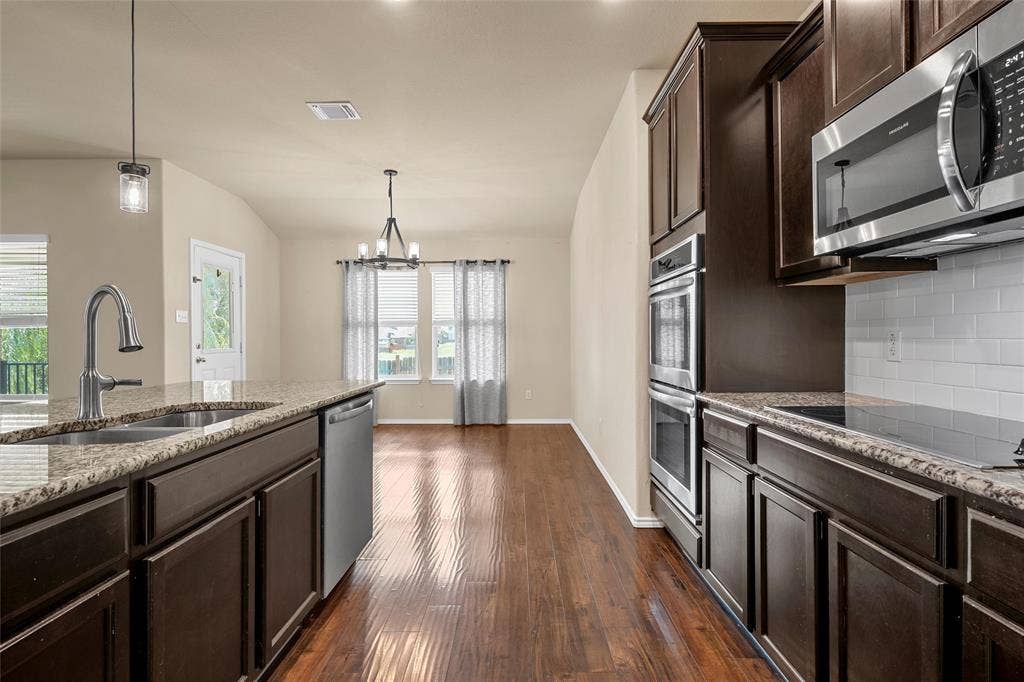 Spacious kitchen featuring rich wood-finish cabinetry, granite countertops, and stainless steel appliances including a built-in double oven and microwave