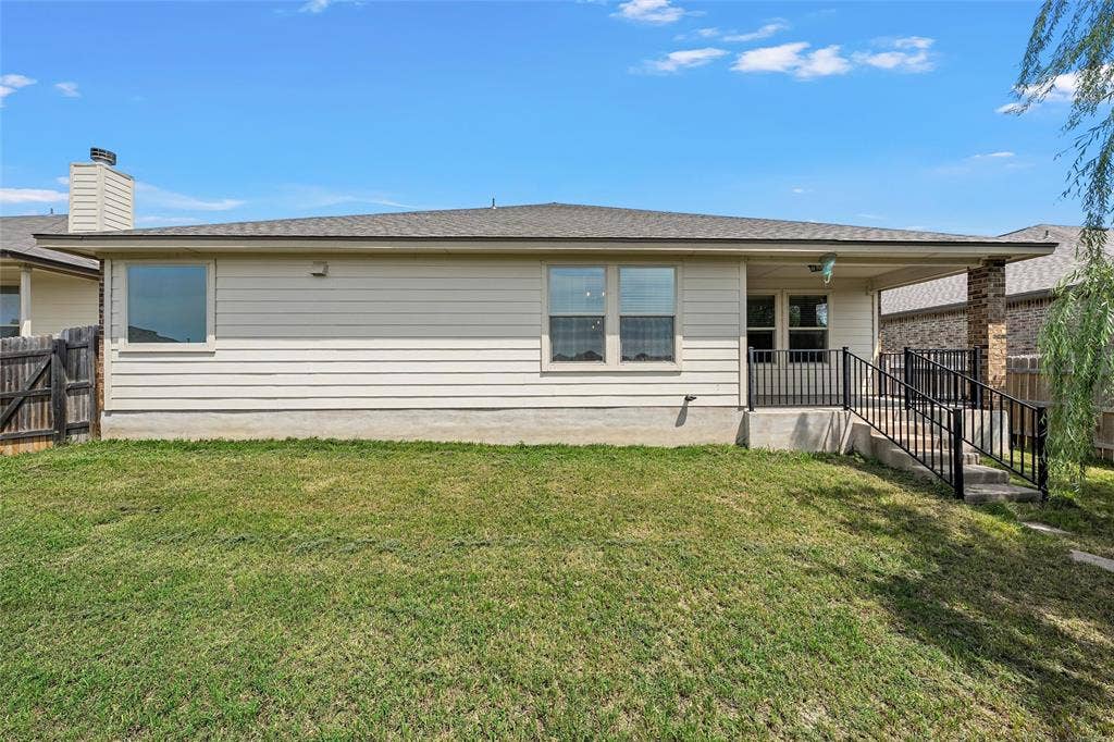 Expansive backyard featuring a manicured lawn, covered patio, concrete steps with black metal railing, and a privacy fence