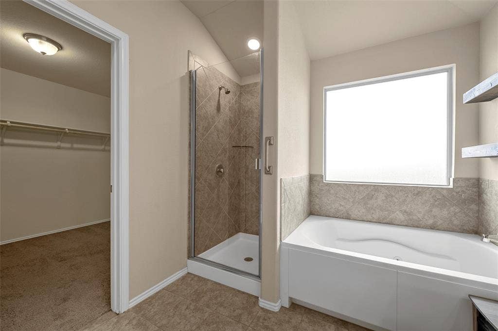 Bathroom featuring a built-in tub, separate shower with glass enclosure, wall-mounted shelving, and a frosted window