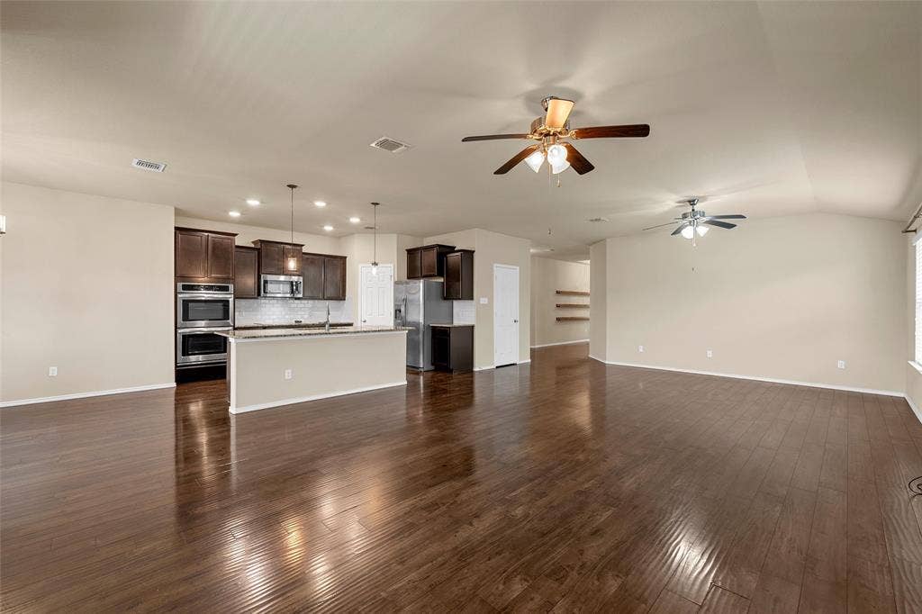 Expansive open concept living area featuring dark wood-finish flooring, two ceiling fans, and neutral wall tones