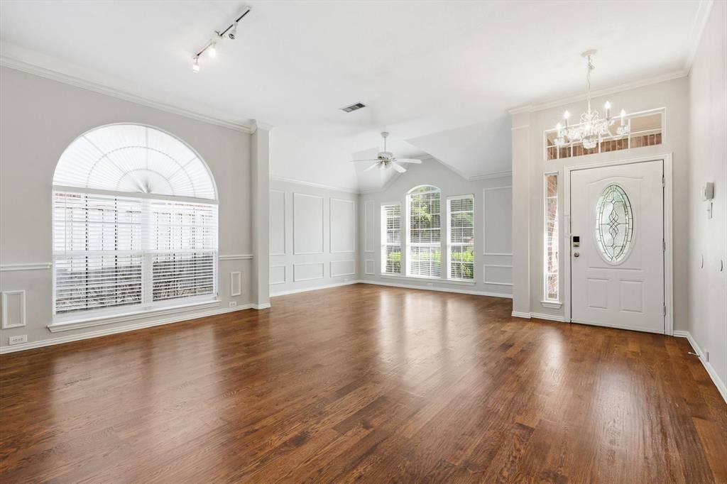 Entryway and living area featuring wood-finish flooring, an arched window with blinds, decorative wall paneling, a vaulted ceiling, and a white front door with an oval leaded glass insert
