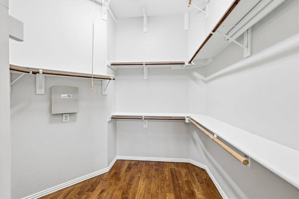 Walk-in closet featuring wood-finish flooring, white walls, white shelving, and hanging rods