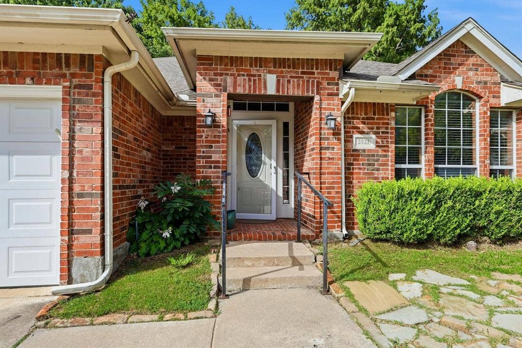 Brick exterior featuring a white garage door, a white entry door with oval glass, an arched window, and a stone walkway