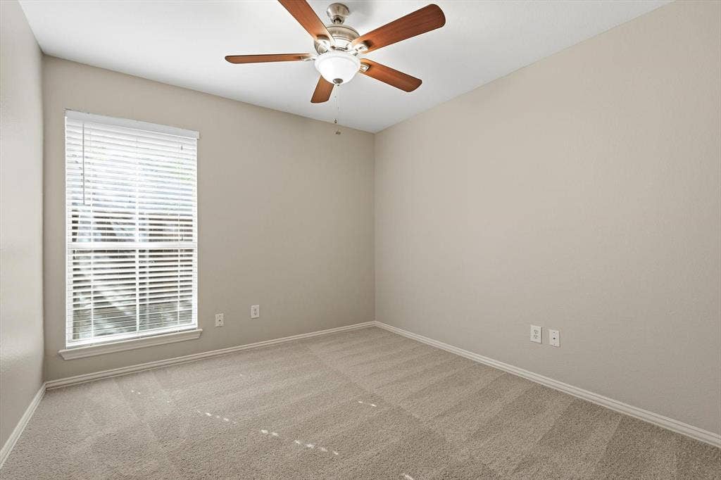 Room featuring neutral carpeting, a large window with horizontal blinds, and a ceiling fan with integrated lighting