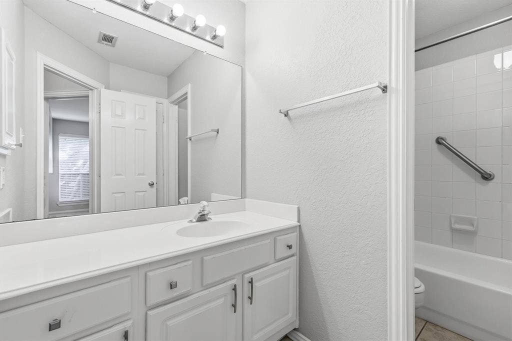 Bathroom featuring a vanity with an integrated sink, a large wall-mounted mirror, a four-bulb vanity light fixture, and a bathtub with white subway tile surround
