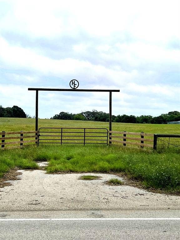 TBD Hwy 59, Athens, TX 75751 Property entrance featuring a metal gate and wooden fence, set against a backdrop of expansive green fields and mature trees