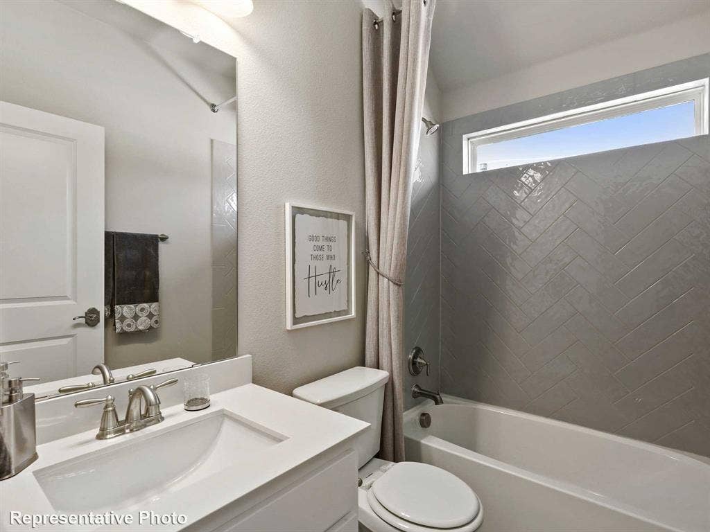 Bathroom featuring a vanity with an integrated sink, a large mirror, and a bathtub with a tiled surround
