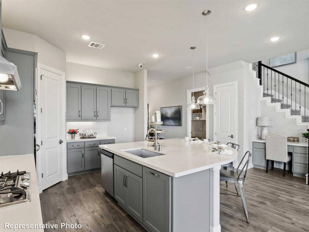 Modern kitchen featuring an expansive island with a built-in sink and seating, gray cabinetry, white countertops, wood-finish flooring, and recessed lighting