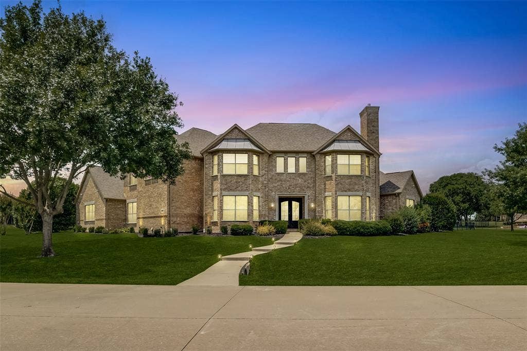 Expansive brick two-story residence featuring a prominent chimney, multiple large windows, and a double-door entry