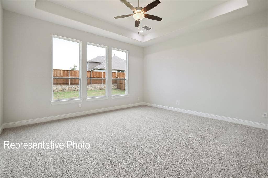 2297 Slate Drive, Waxahachie, TX 75167 Spacious room featuring light-colored carpeting, three tall windows, a tray ceiling, and a ceiling fan with integrated lighting