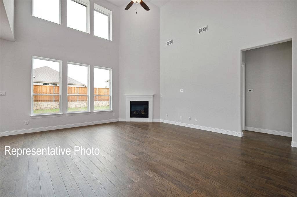 2297 Slate Drive, Waxahachie, TX 75167 Two-story living area featuring tall windows, a corner fireplace with a white mantel, and dark wood-finish flooring