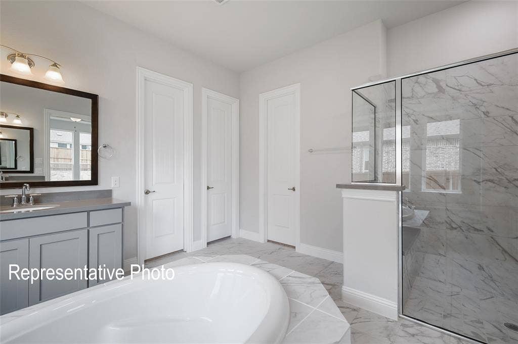 2297 Slate Drive, Waxahachie, TX 75167 Spacious bathroom featuring a glass-enclosed shower with marble-look tile, a separate built-in soaking tub, and a vanity with a rectangular sink and gray cabinetry