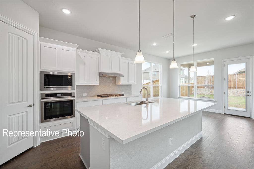 2297 Slate Drive, Waxahachie, TX 75167 Modern kitchen featuring a large central island with a sink, white cabinetry, stainless steel appliances, and wood-finish flooring