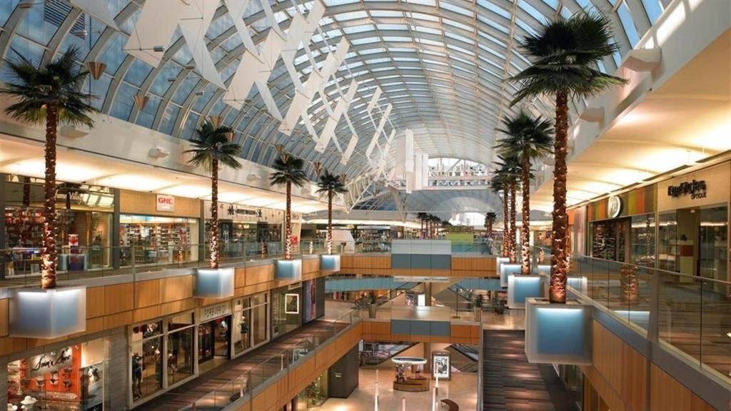 Multi-level retail interior featuring a vaulted glass ceiling and integrated palm trees