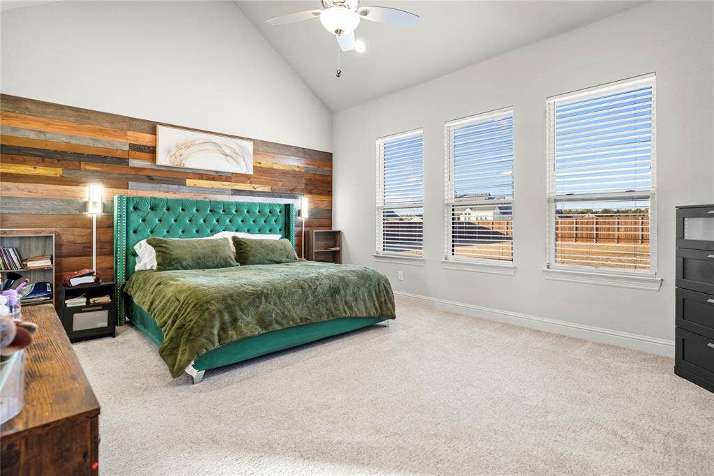 Spacious room featuring vaulted ceilings, light-colored carpeting, and a prominent wood-panel accent wall