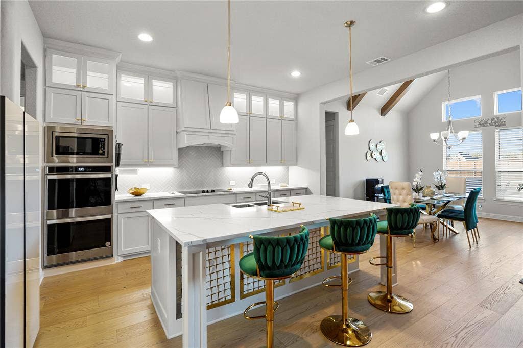 Gourmet kitchen with an expansive island featuring a waterfall-edge countertop, under-cabinet lighting, a built-in double oven, and a herringbone tile backsplash
