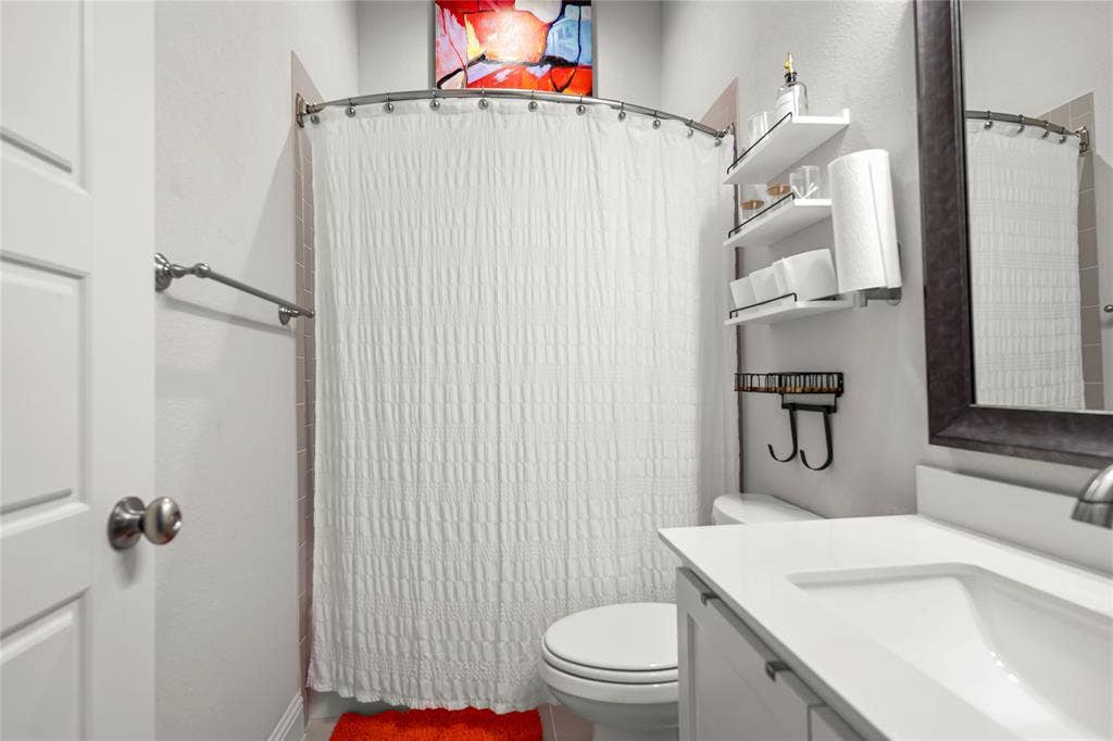 Bathroom featuring a white vanity with an integrated sink, framed mirror, and a curved shower rod