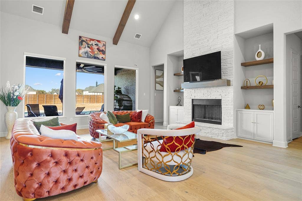 Soaring vaulted ceiling with exposed cedar beams, floor-to-ceiling stone fireplace with built-in shelving and hardwood floors.