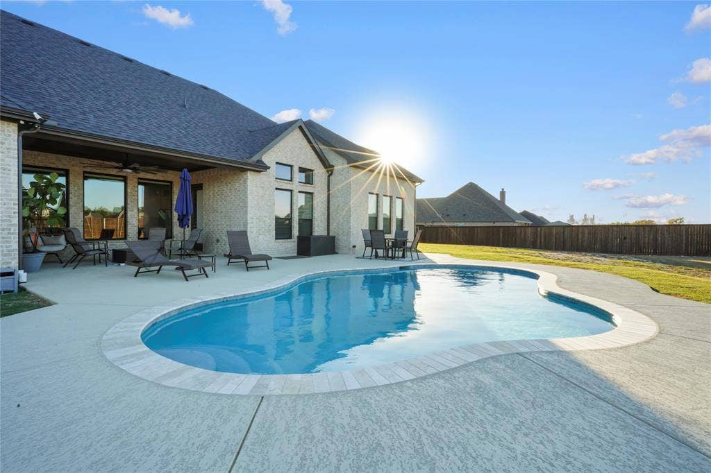Freeform swimming pool with concrete decking, featuring a covered patio and a brick exterior