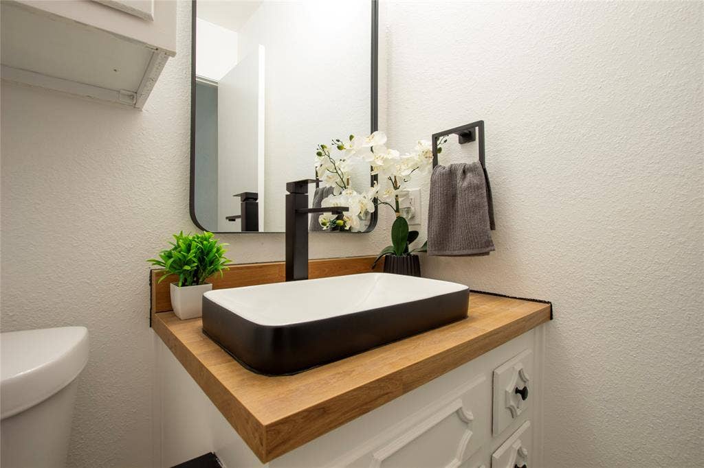 1205 Augusta Road, Benbrook, TX 76126 Powder room featuring a rectangular vessel sink with a matte black faucet, a wood-finish countertop, and a contemporary wall mirror