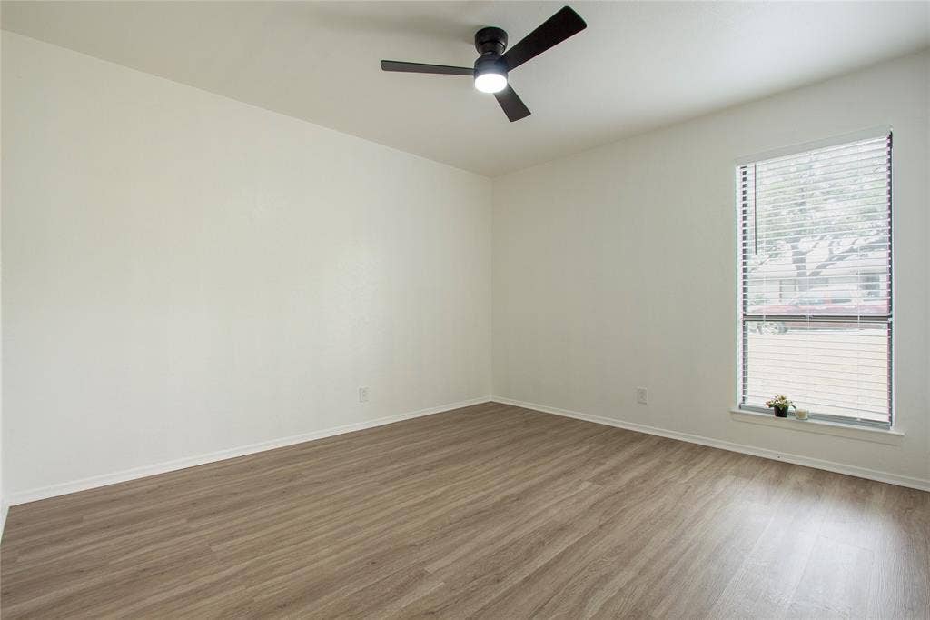 1205 Augusta Road, Benbrook, TX 76126 Spacious room featuring wood-finish flooring, a contemporary ceiling fan with integrated lighting, a large window with horizontal blinds, and white baseboards
