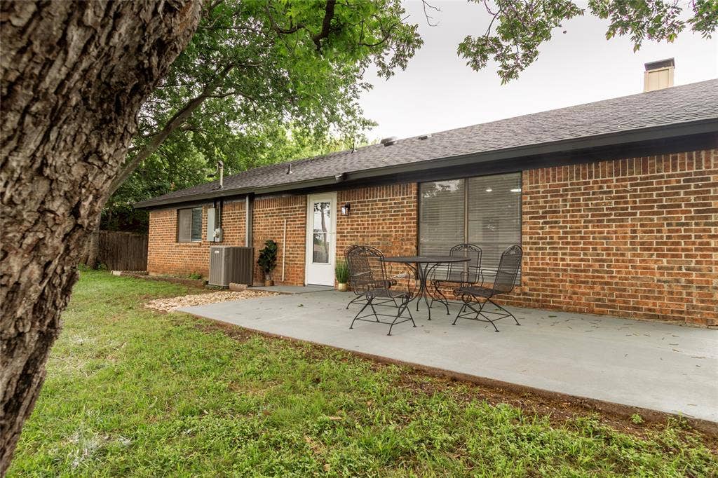 1205 Augusta Road, Benbrook, TX 76126 Backyard featuring a red brick exterior, a grey concrete patio, and a dark shingle roof