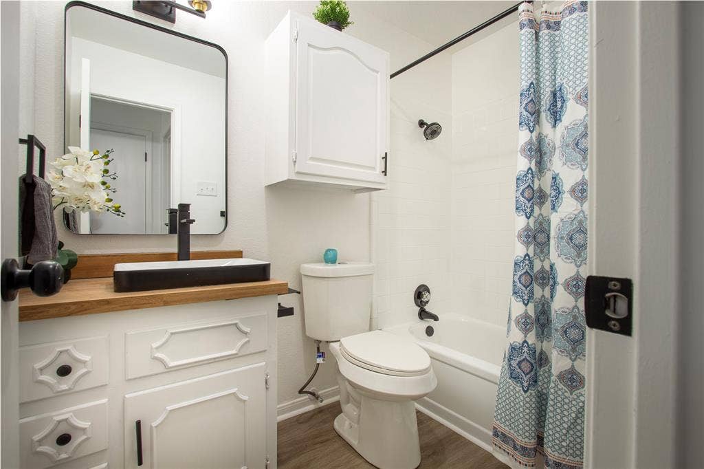 1205 Augusta Road, Benbrook, TX 76126 Bathroom featuring a vessel sink with a dark faucet, wood-finish countertop, and white cabinetry